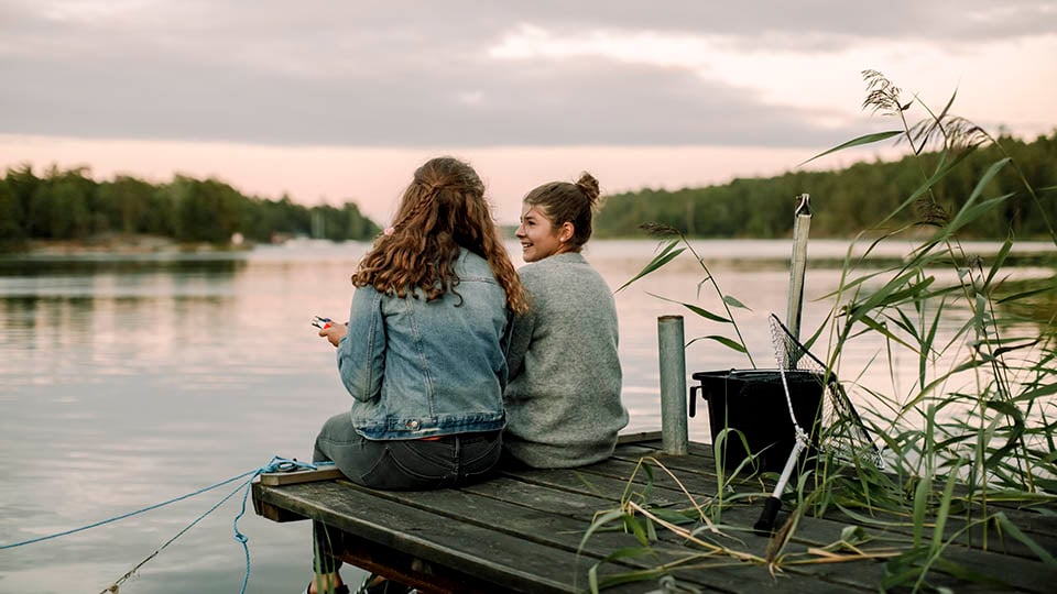 Tv&aring; ungdomar sitter p&aring; en brygga vid en sj&ouml;