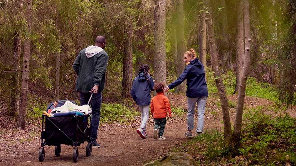 Familj med tv&aring; barn promenerar i skogen och drar en campingvagn efter sig. Sverige