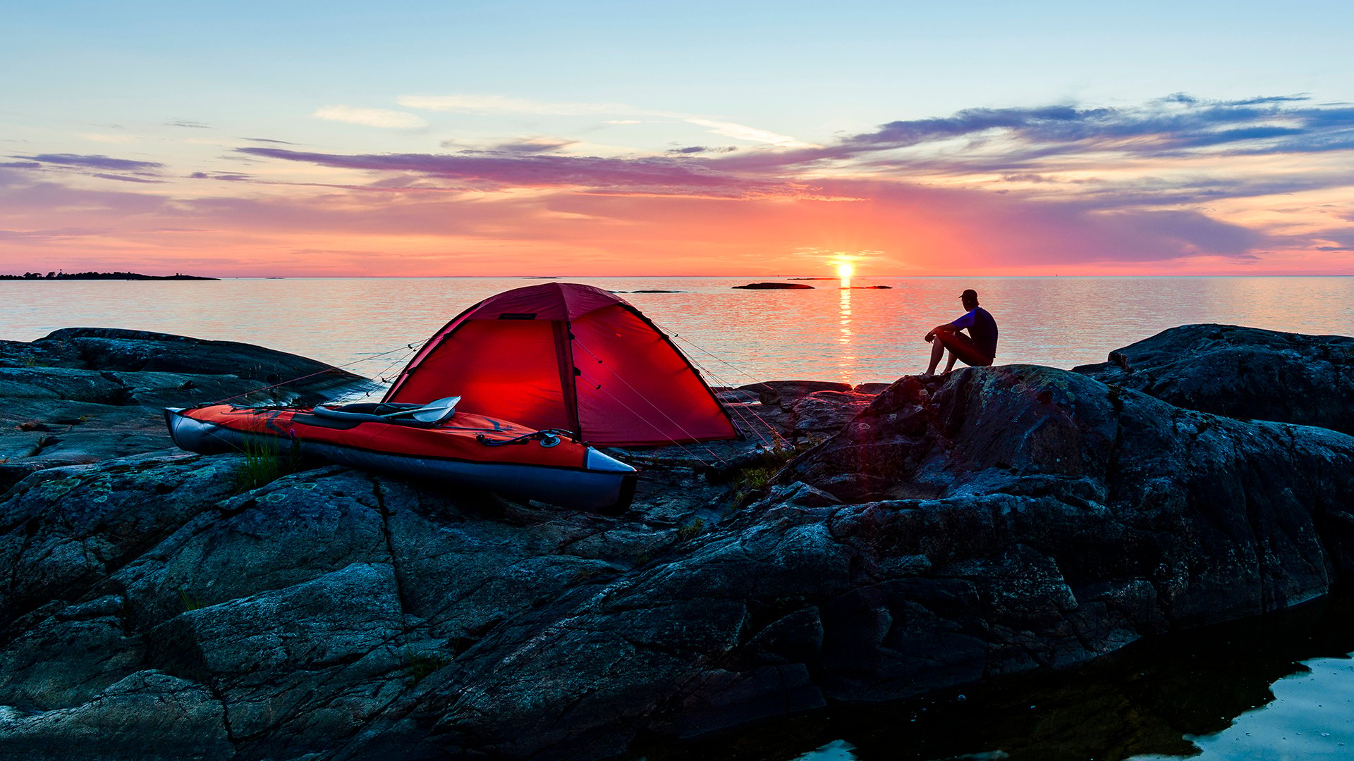 Man sitter vid upplyst tält vid Vänern (Ekens skärgård).